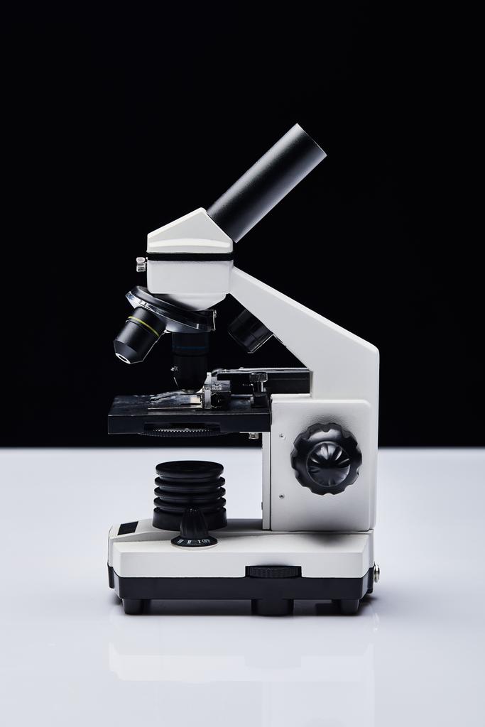 σύγχρονο μικροσκόπιο σε λευκό τραπέζι απομονωμένο σε μαύρο - Φωτογραφία, εικόνα
