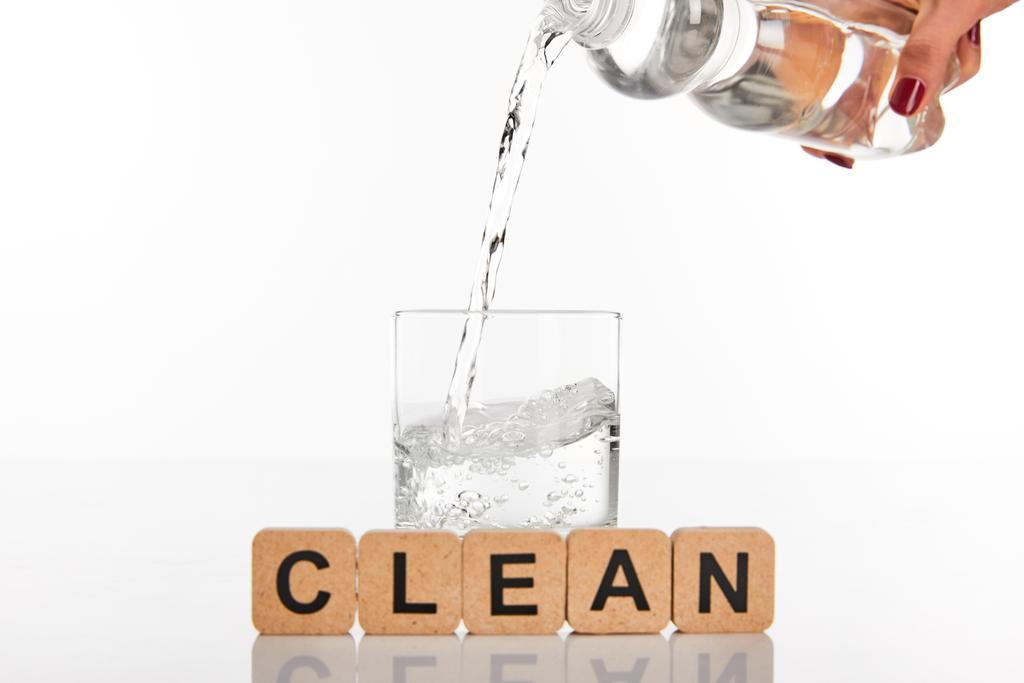 bijgesneden beeld van vrouw gieten water uit fles in glas in de buurt van kubussen met schone belettering geïsoleerd op wit - Foto, afbeelding