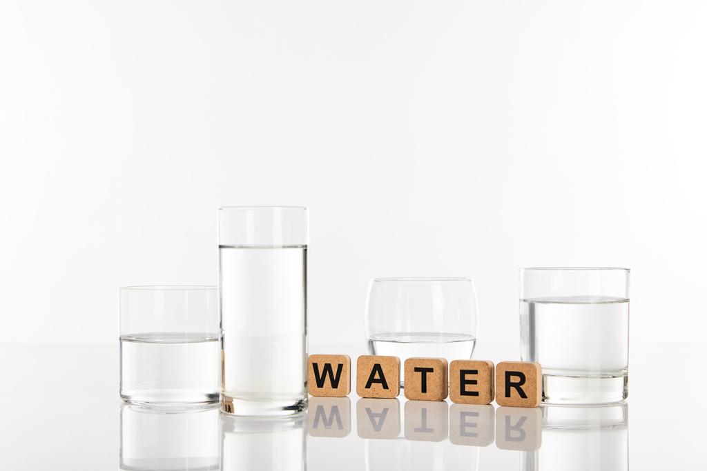 klares Süßwasser in Gläsern in der Nähe von Würfeln mit Wasseraufdruck isoliert auf weiß - Foto, Bild