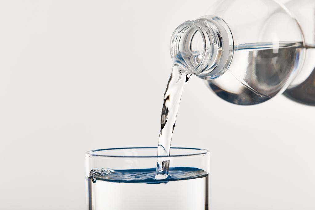 tiszta, friss víz ömlik az üvegbe a fehér üvegből izolált palackból - Fotó, kép