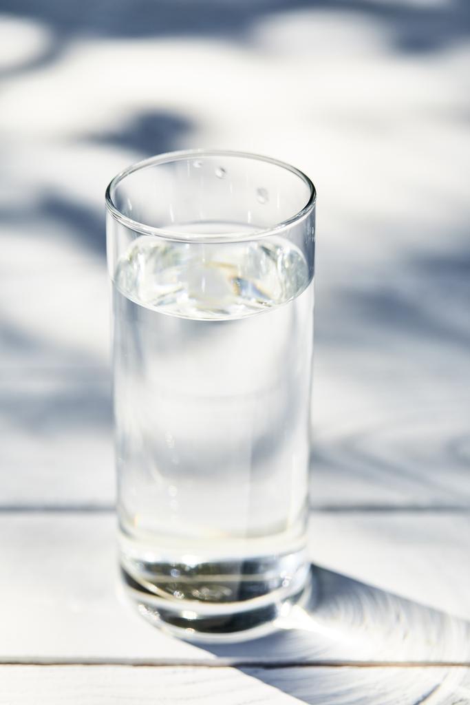 słodka czysta woda w przezroczystym szkle w słoneczny dzień na białym drewnianym stole - Zdjęcie, obraz