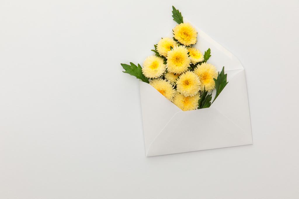 bovenaanzicht van gele asters in envelop op witte achtergrond met kopieerruimte - Foto, afbeelding