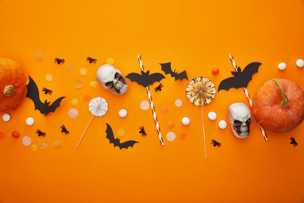 bovenaanzicht van pompoen, schedels, vleermuizen en spinnen met confetti op oranje achtergrond, Halloween decoratie - Foto, afbeelding