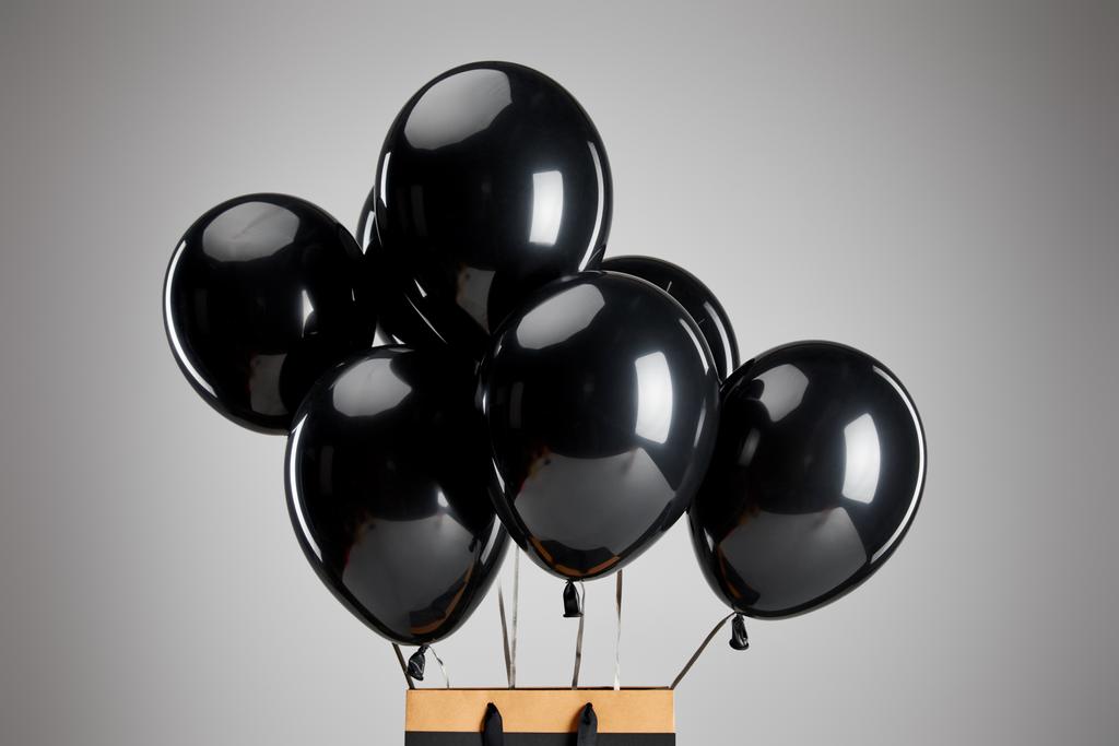 Куча черных воздушных шаров с бумажным пакетом для покупок, изолированных на серой черной пятничной концепции
 - Фото, изображение