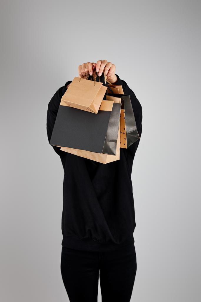 žena s nejasným obličejem držící papírové nákupní tašky izolované na šedém, černém pátečním konceptu - Fotografie, Obrázek