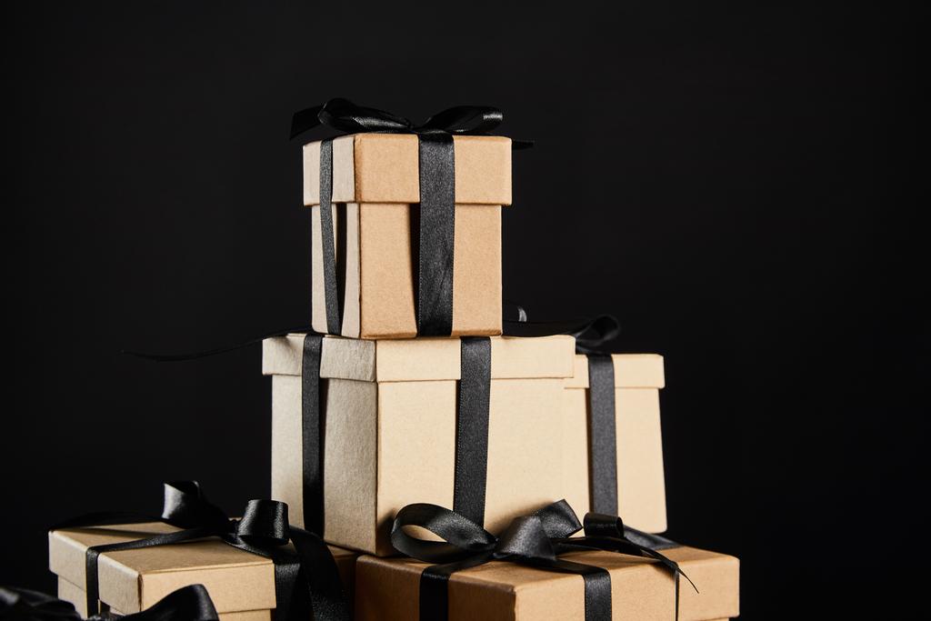 stapel kartonnen geschenkdozen met zwarte linten geïsoleerd op zwart, zwart vrijdag concept - Foto, afbeelding
