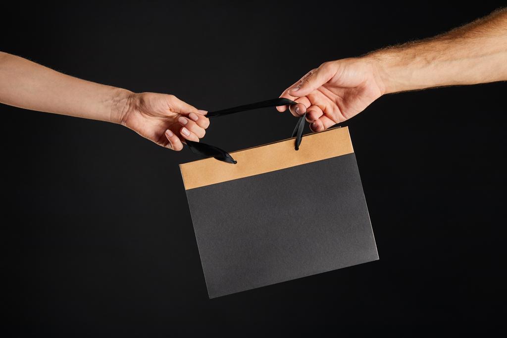 vista recortada de la mujer y el hombre sosteniendo bolsa de compras de papel aislado en negro, concepto de viernes negro
 - Foto, imagen
