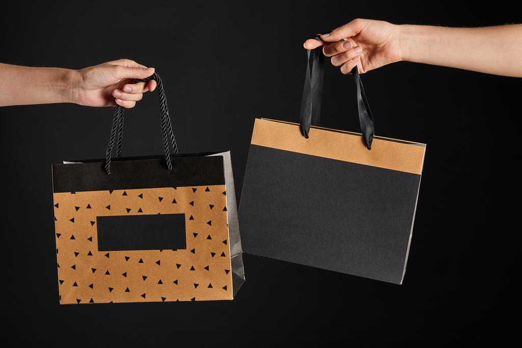частичный взгляд женщины и мужчины, держащих бумажные пакеты покупки изолированы на черной, черной концепции пятницы
 - Фото, изображение