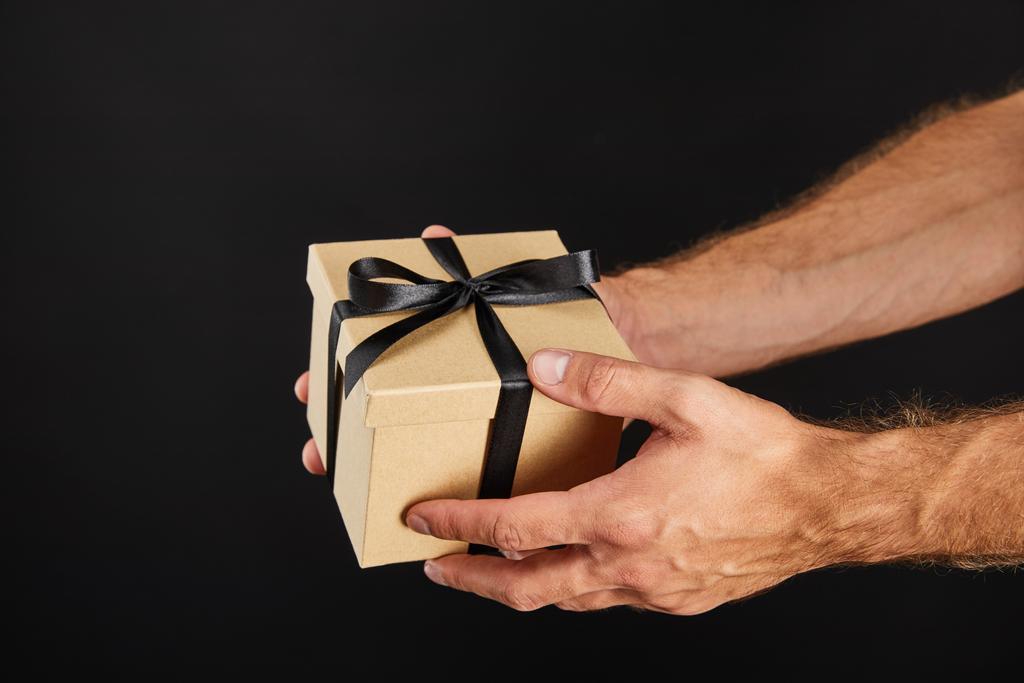 cropped άποψη του ανθρώπου κρατώντας χαρτονένιο κουτί δώρου με κορδέλα απομονώνονται σε μαύρο, μαύρο Παρασκευή έννοια - Φωτογραφία, εικόνα