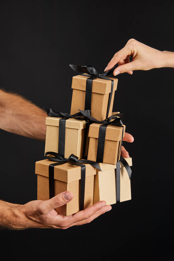обрізаний вид чоловіка і жінки, що тримає картонні подарункові коробки зі стрічками ізольовані на чорній, чорній концепції п'ятниці
 - Фото, зображення