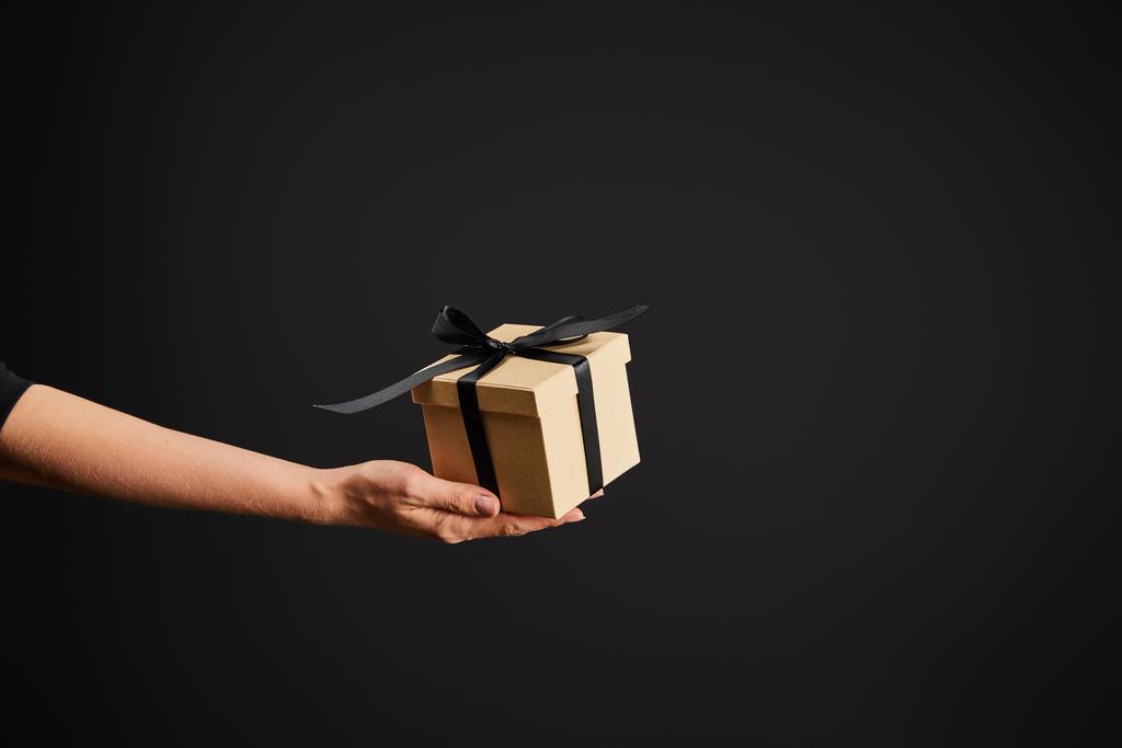 cropped view of woman holding cardboard gift box with ribbon isolated on black, black Friday concept - Photo, Image