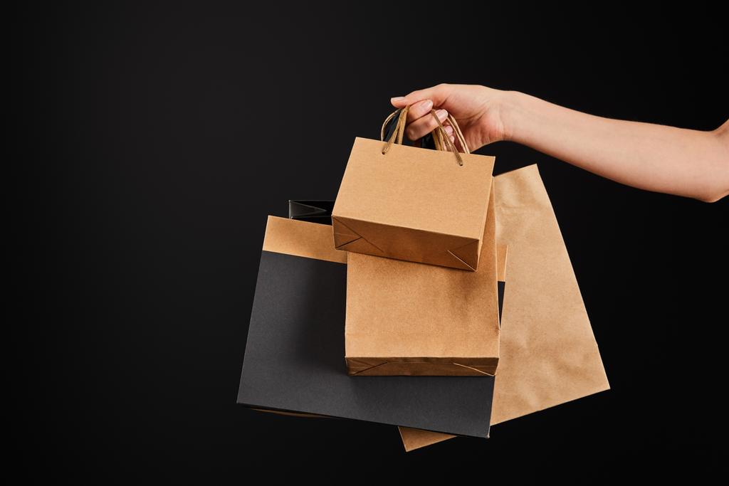 gedeeltelijk uitzicht op vrouw met papieren boodschappentassen geïsoleerd op zwart, zwart vrijdag concept - Foto, afbeelding