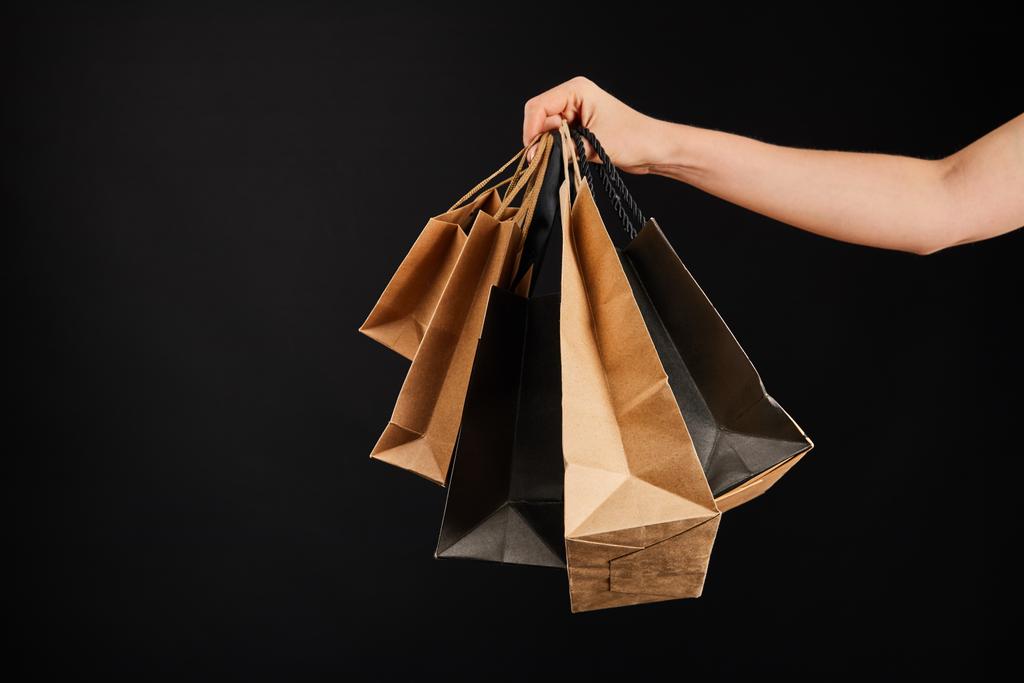 częściowy widok kobiety trzymającej papierowe torby na zakupy odizolowane od czarnej, czarnej koncepcji piątek - Zdjęcie, obraz