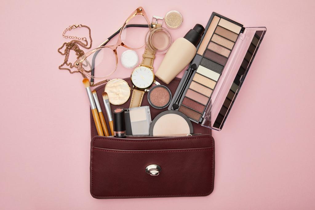 top view barna táska közelében dekoratív kozmetikumok és óra elszigetelt rózsaszín  - Fotó, kép