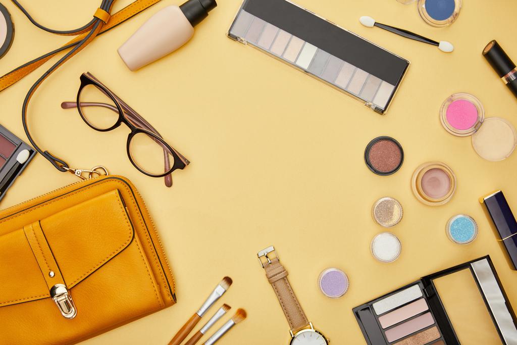 vista superior de la bolsa cerca de cosméticos decorativos y gafas aisladas en amarillo
  - Foto, Imagen