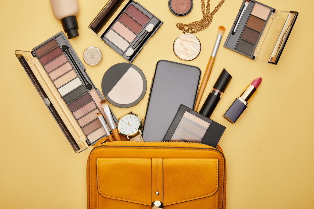 top view of bag with decorative cosmetics and smartphone with blank screen isolated on yellow  - Photo, Image