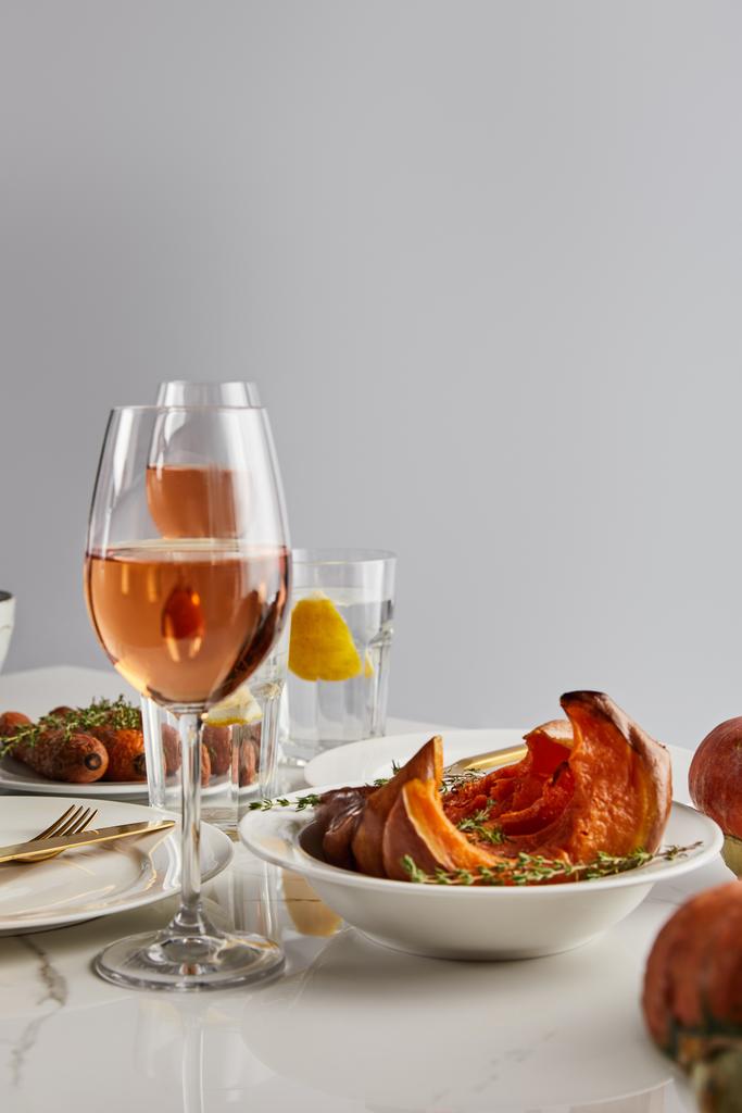 Gläser mit Rosenwein, gebackenem Kürbis und Möhren serviert auf weißem Marmortisch isoliert auf grau - Foto, Bild