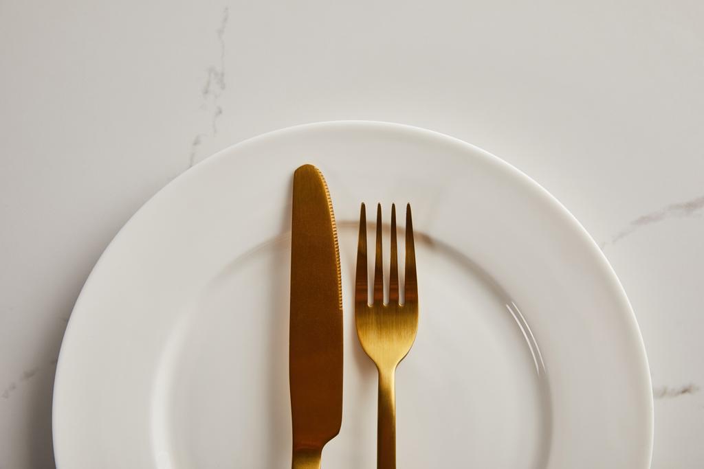 vista superior de cuchillo de oro y tenedor en placa blanca limpia sobre mesa de mármol
 - Foto, imagen