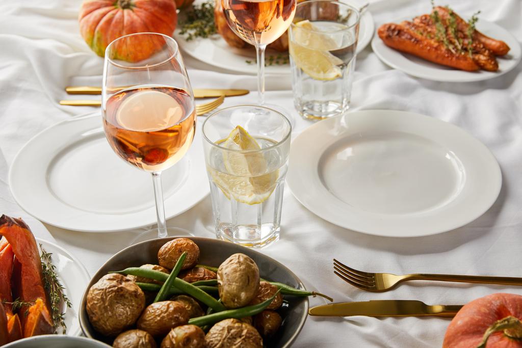dîner d'action de grâce festif avec des légumes cuits au four et des verres avec du vin de rose et de l'eau de citron sur une nappe blanche
 - Photo, image