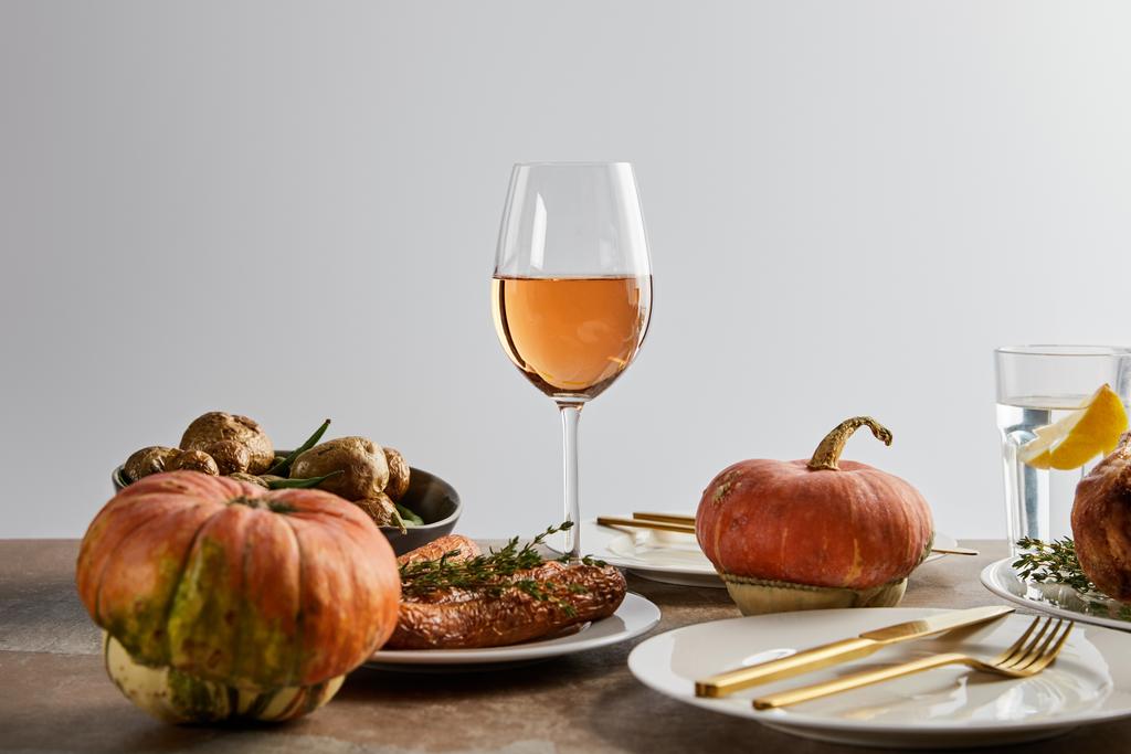 whole pumpkins near baked potatoes and carrots, and glasses with rose wine and lemon water isolated on grey - Photo, Image