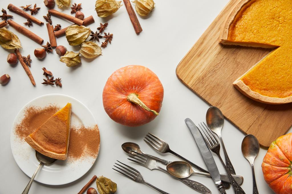 top view of delicious pumpkin pie near whole pumpkin, spices and cutlery on white marble surface - Photo, Image