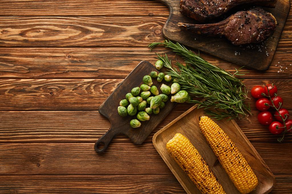 Draufsicht auf Fleisch, Mais, Kirschtomaten, Grün, Rosenkohl auf Schneidebrett  - Foto, Bild