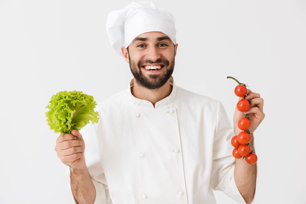 Image of happy chef man in cook hat smiling while holding tomato - Photo, Image