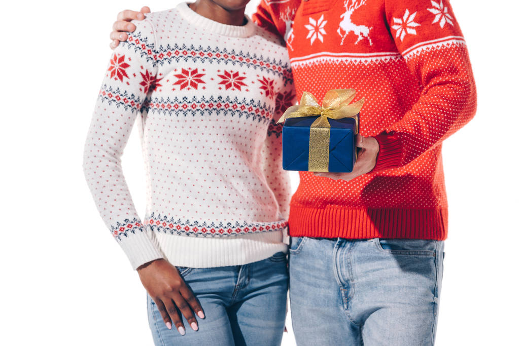 abgeschnittene Ansicht eines gemischtrassigen Paares in Winterpullovern mit Weihnachtsgeschenk, isoliert auf weiß - Foto, Bild