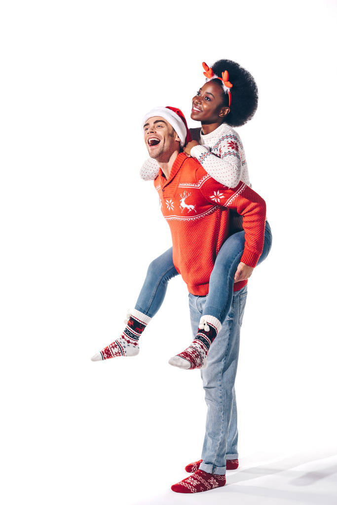 multikulturelles Paar mit Weihnachtsmann und Hirschhörnern huckepack, isoliert auf weiß - Foto, Bild