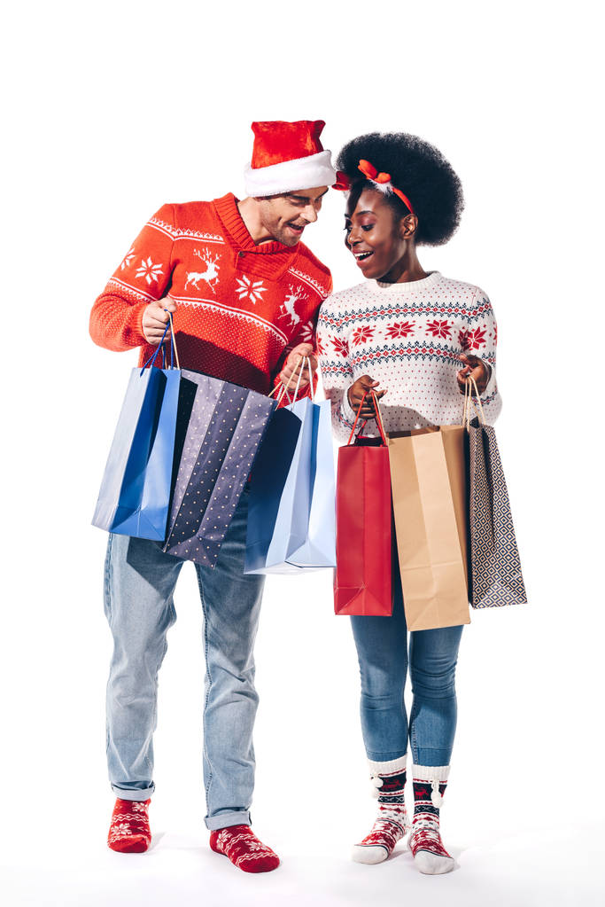 junges multikulturelles Paar mit Weihnachtsmann und Hirschhörnern in Einkaufstaschen, isoliert auf weißem Grund - Foto, Bild