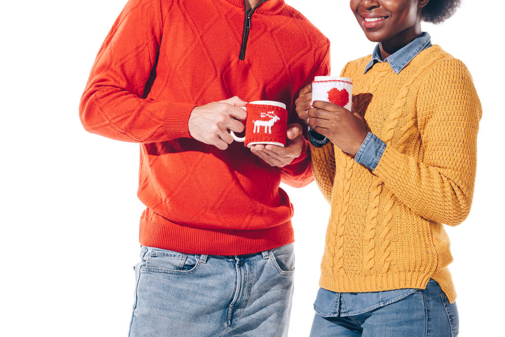 обрезанный вид счастливой многонациональной пары в шляпе Санты и оленьих рогах, пьющих кофе, изолированных на белом
 - Фото, изображение