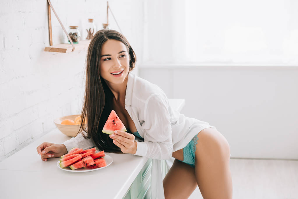 красивая девушка в нижнем белье и белой рубашке едят арбуз на кухне
 - Фото, изображение