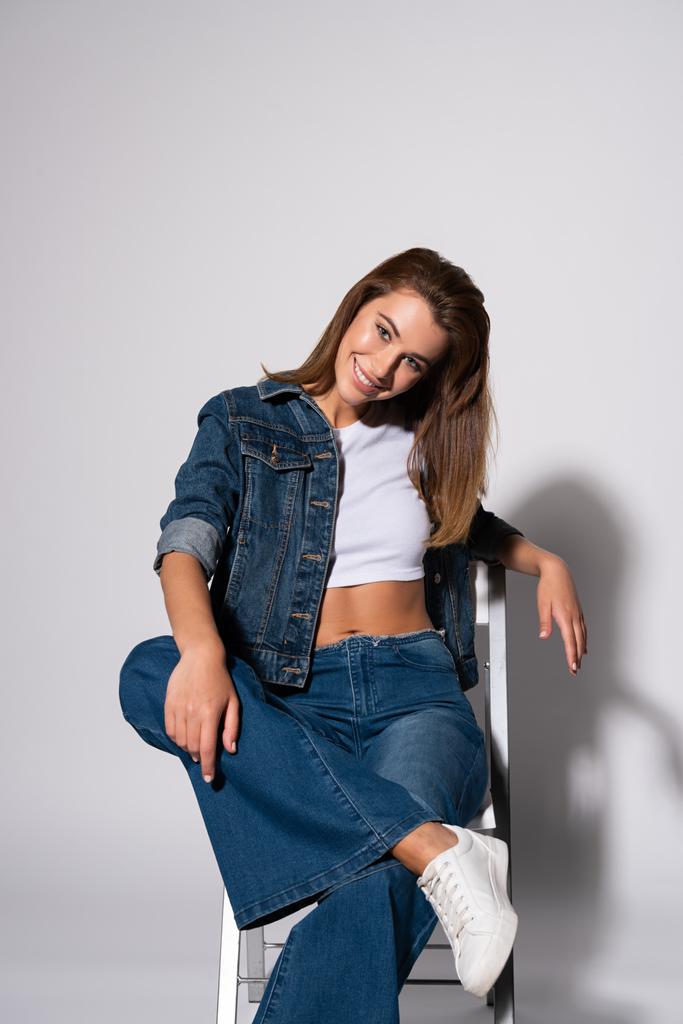 menina alegre em jeans jeans sentados na cadeira no branco
  - Foto, Imagem
