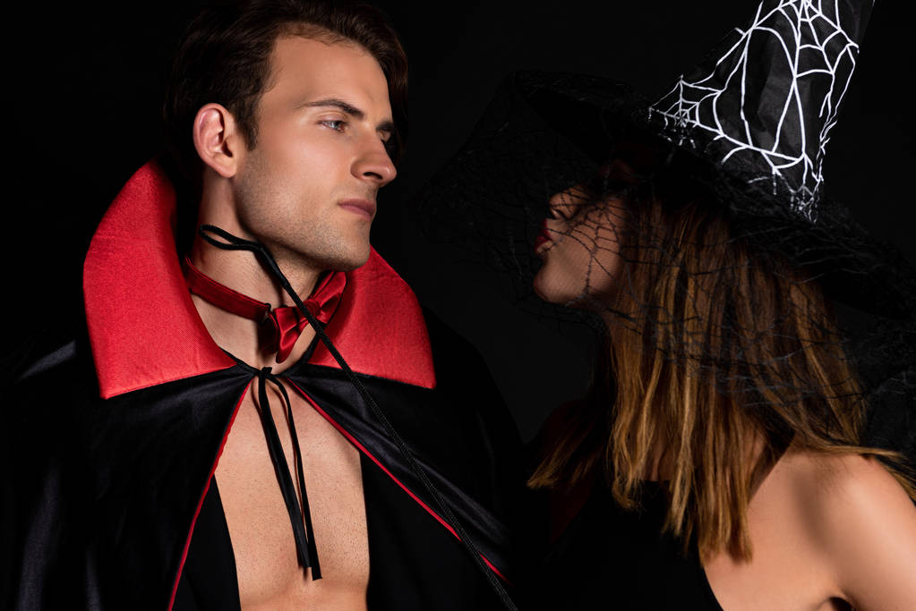 женщина в шапке ведьмы с утиным лицом, смотрящая на мужчину в костюме Хэллоуина, изолированном на черном
  - Фото, изображение