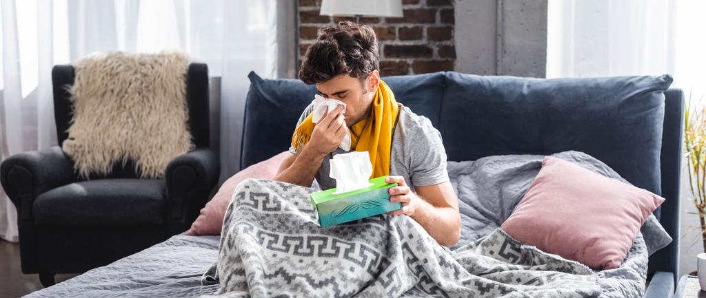 панорамный снимок больного человека в шарфе чихающего и держащего салфетку
  - Фото, изображение