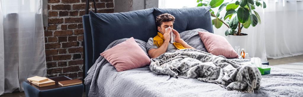 Panoramaaufnahme eines kranken Mannes mit Schal, der niest und im Bett liegt  - Foto, Bild