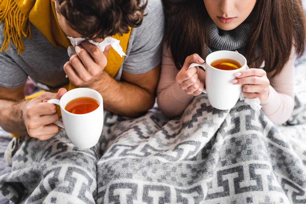 Ausgeschnittener Blick auf kranke Freundin und Freund, die Tassen halten und mit Tee niesen  - Foto, Bild