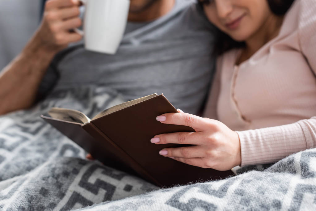 cropped view of girlfriend reading book and boyfriend holding cup of tea  - Photo, Image