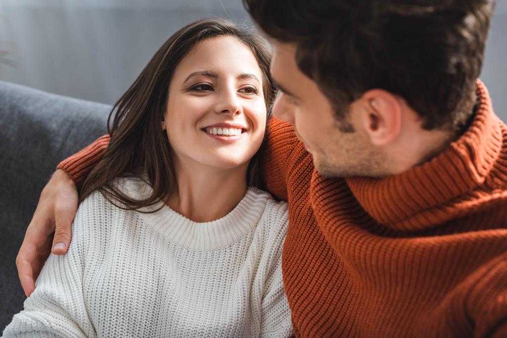 atractiva novia y novio en suéteres sonriendo y abrazándose en el apartamento
  - Foto, imagen