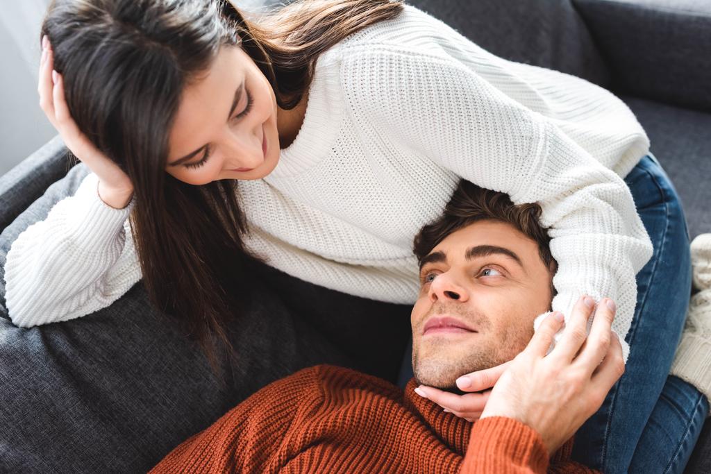 φίλος ξαπλωμένος στα γόνατα της ελκυστικής φίλη σε πουλόβερ και χαμογελώντας στο διαμέρισμα  - Φωτογραφία, εικόνα