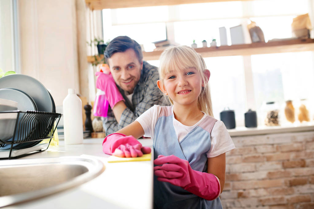 Χαρούμενο κορίτσι που φοράει ροζ γάντια που βοηθάει τον μπαμπά με την καθαριότητα. - Φωτογραφία, εικόνα