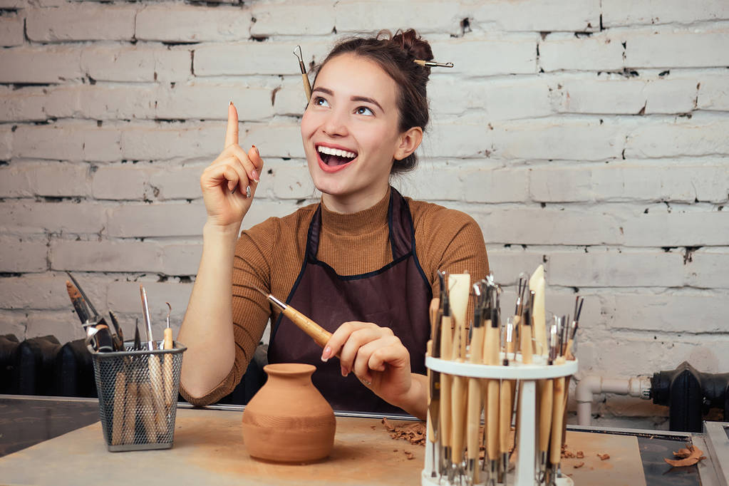 Porträt einer jungen, fröhlichen Frau mit einer Vase aus Ton. Der Töpfer stellt am Tisch in einer Töpferei eine Vase her. Konzept der Inspiration und Ideen - Foto, Bild