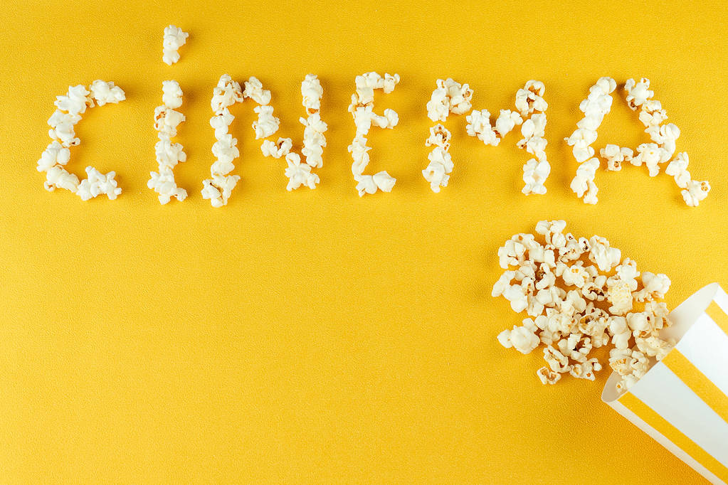 palomitas de maíz esparcidas de un papel rayado en un cine de inscripciones de fondo amarillo. el concepto de cine en casa y películas en el cine
 - Foto, imagen