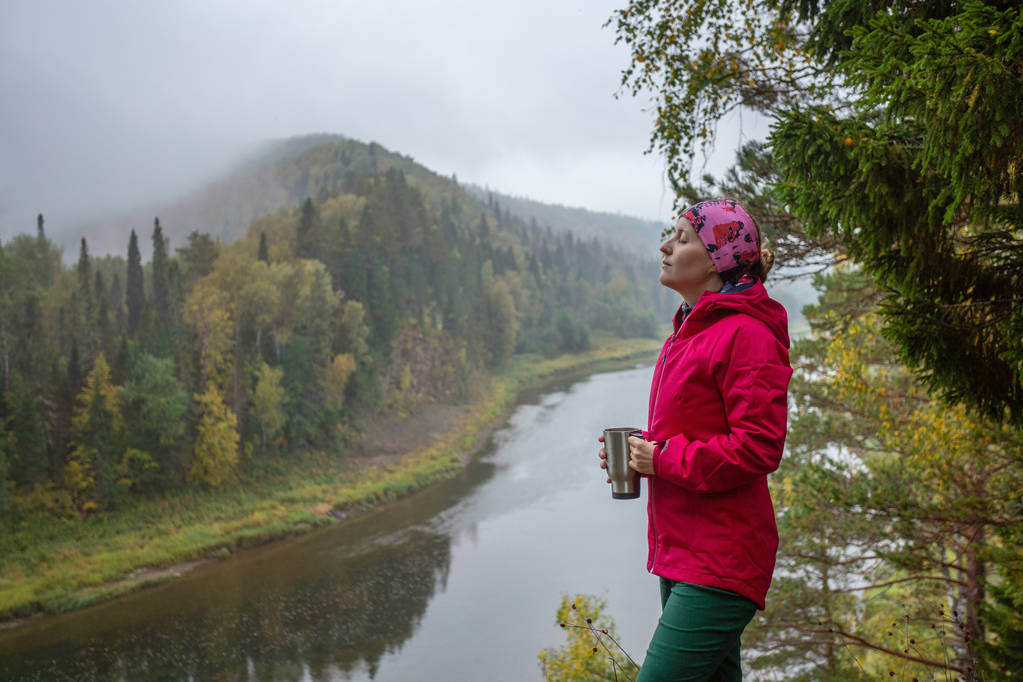 paesaggio autunnale. Giovane turista donna in piedi sulla riva del fiume con una tazza di tè. guardando il fiume. campeggio in autunno - Foto, immagini