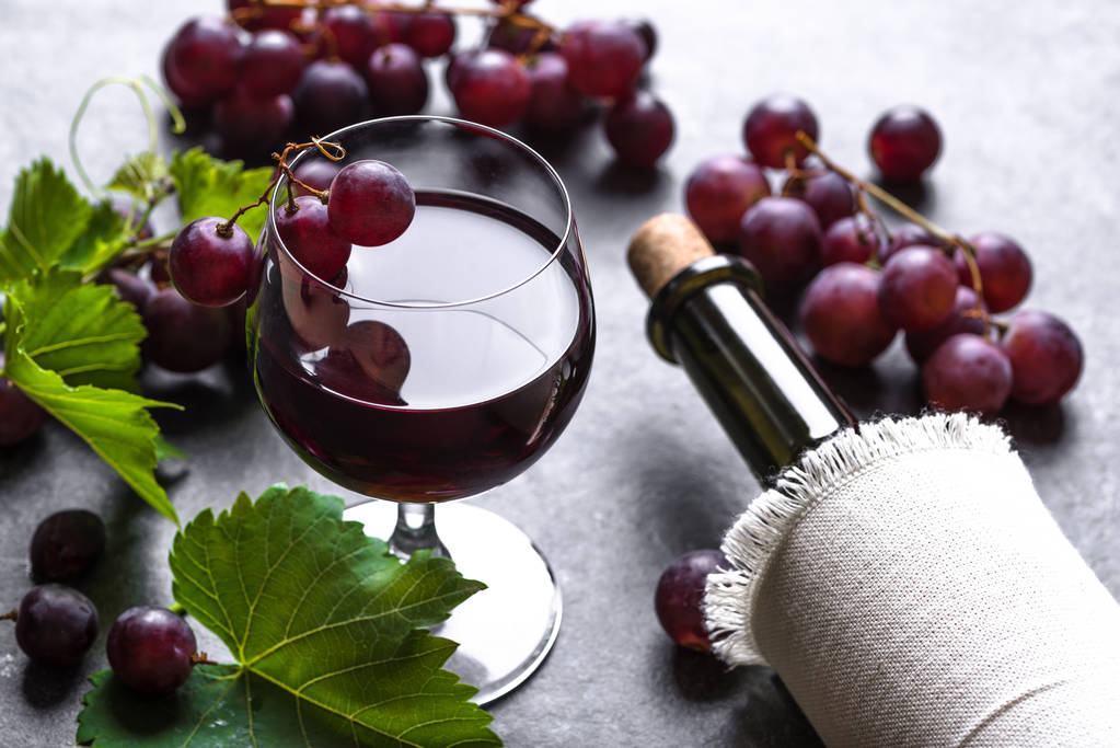 Glas Wein mit roten Trauben und Weinflasche auf dunklem Hintergrund - Foto, Bild