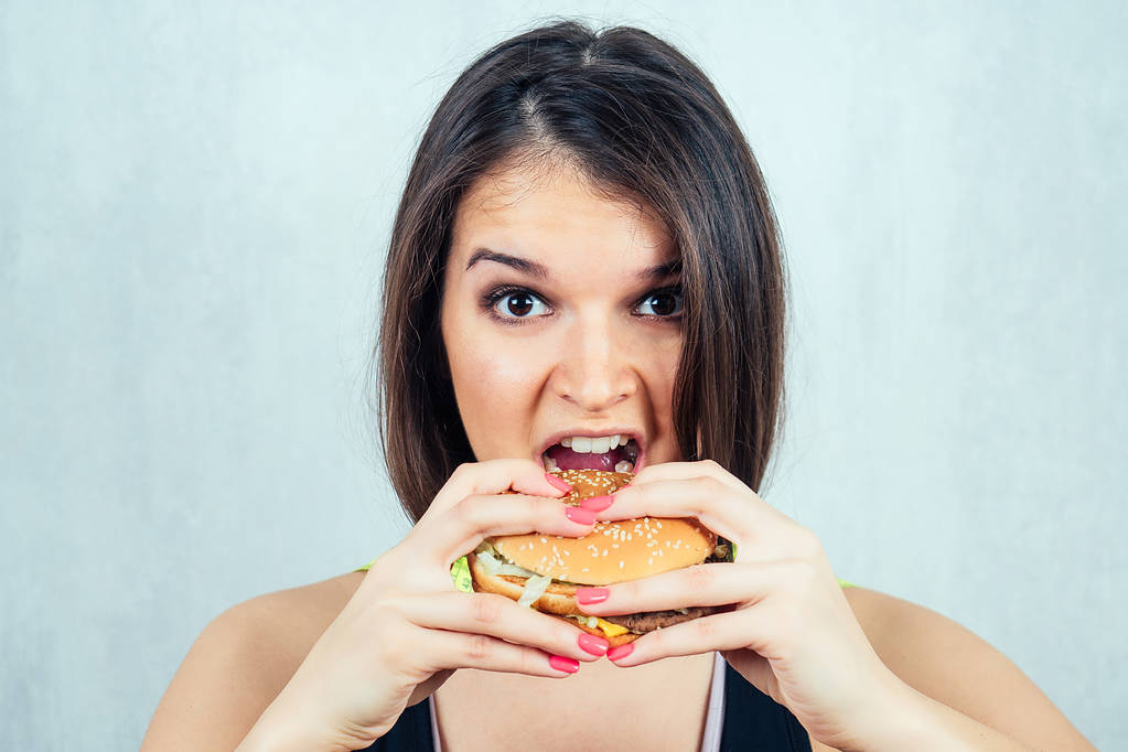 νέα και ελκυστική γυναίκα σε μαύρο T-shirt και ταινία μέτρησης τρώει ένα burger υψηλής θερμίδων - Φωτογραφία, εικόνα