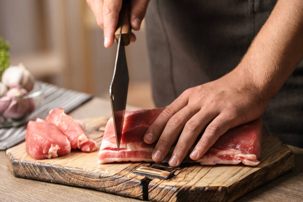Чоловік ріже свіже сире м'ясо на столі на кухні, крупним планом
 - Фото, зображення