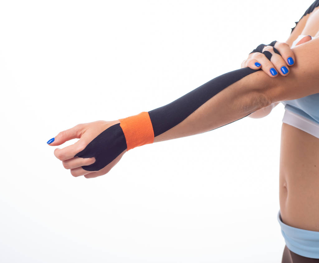 Een vrouwelijke atleet zet een kineziotape op haar pols. Kineziologie, alternatieve behandeling voor verwondingen van gewrichten en pezen. Fysiotherapie van chronische ontsteking van de gewrichten van een Womans arm. - Foto, afbeelding