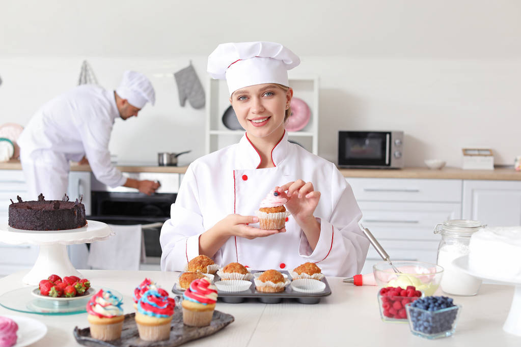 Confiseur féminin décorant cupcake savoureux dans la cuisine
 - Photo, image