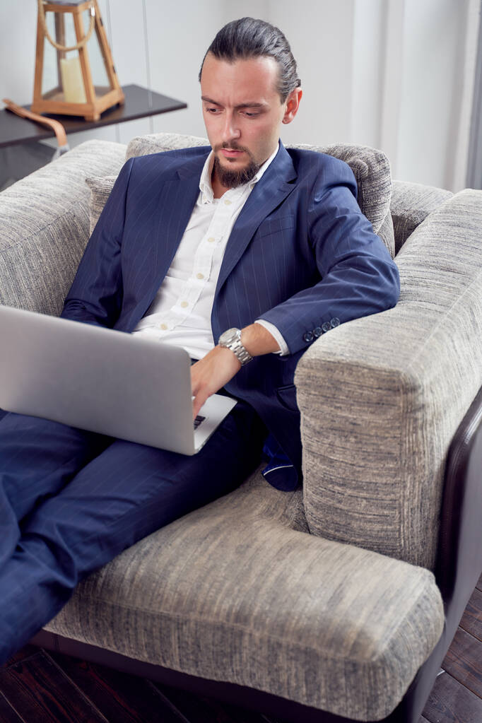 Foto eines seriösen Geschäftsmannes mit Laptop auf Sofa im Zimmer - Foto, Bild